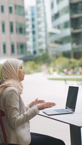 Vertikales-Video-Einer-Muslimischen-Geschäftsfrau,-Die-Draußen-In-Stadtgärten-Sitzt-Und-Ein-Video-Von-Einem-Anruf-Auf-Laptop-2-Macht